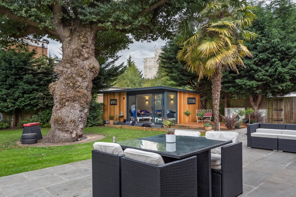 Exterior of a TGO1 pilates studio with a large tree in front and a black cockapoo and rattan garden furniture in the foreground