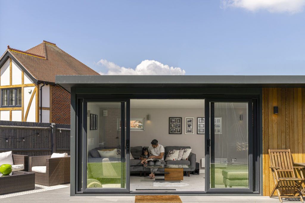 Exterior of a garden room on a patio with garden furniture to the left and a father and daughter sitting inside the garden room