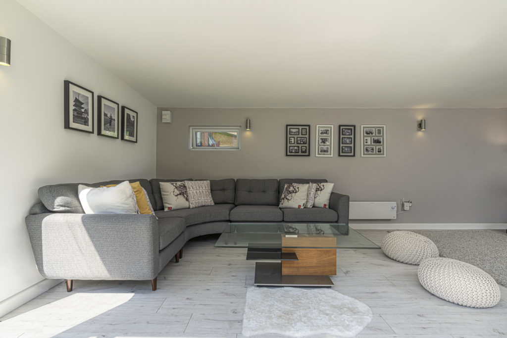 Interior of a garden room with a grey L shaped sofa, coffee table and photos on the back wall